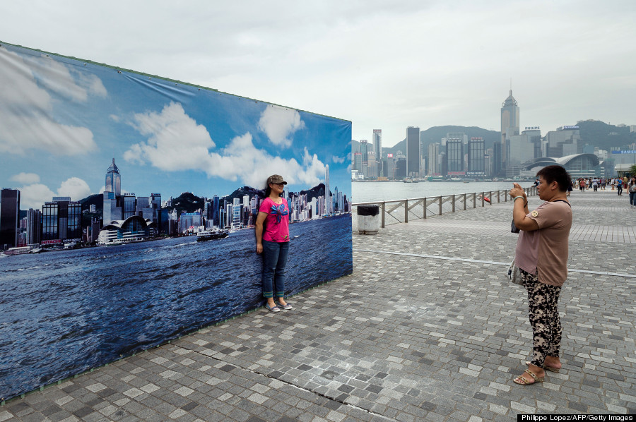 A tourist has her picture taken during a cloudy day in front of a billboard featuring photos of the city skyline with a clear sky in Hong Kong on August 30, 2013. The billboard erected along the Avenue of Stars attracts tourists who find it more appealing to pose for photographs in front of it than the city's skyline on a cloudy or polluted day.   AFP PHOTO / Philippe Lopez        (Photo credit should read PHILIPPE LOPEZ/AFP/Getty Images)